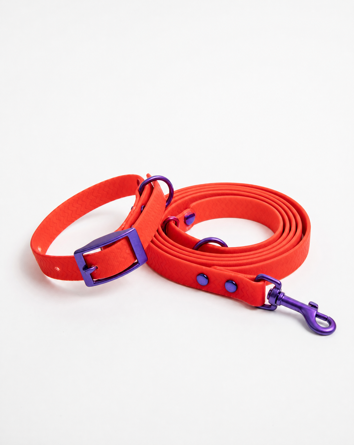 A bright red dog collar and matching lead rope set with shiny purple hardware, photographed on a clean white background.