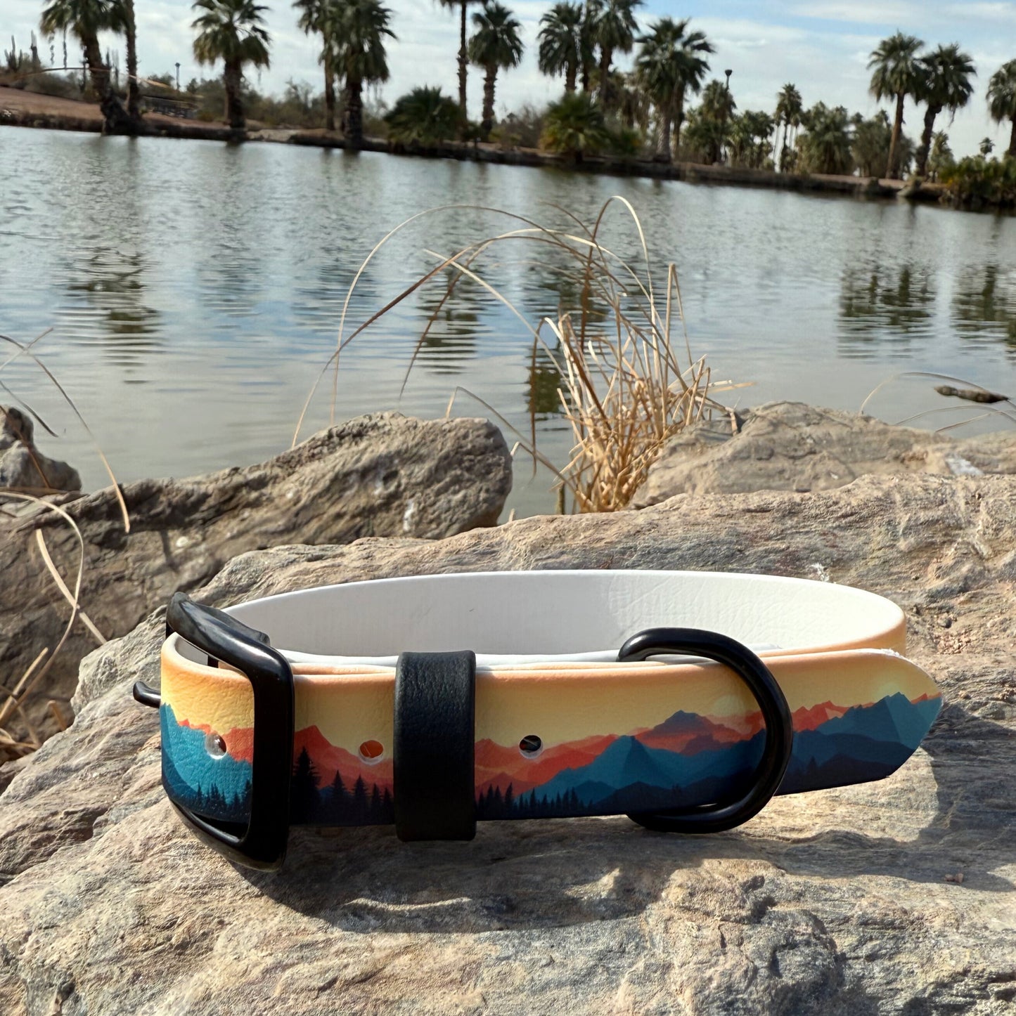 A biothane collar with a mountains and sunset design, displayed on a rock with a body of water and trees in the background.