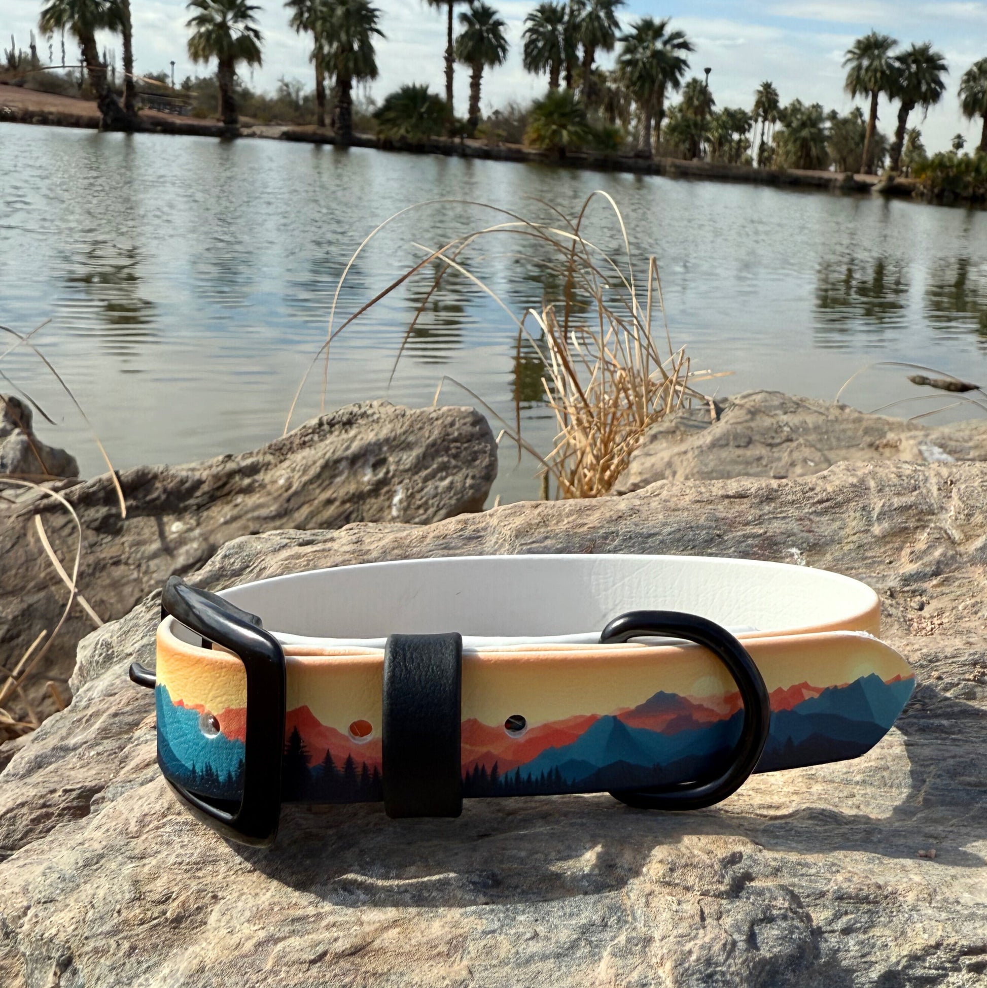 A biothane collar with a mountains and sunset design, displayed on a rock with a body of water and trees in the background.