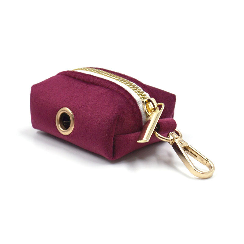Burgundy velvet poop bag dispenser with gold zipper and clip on a white background