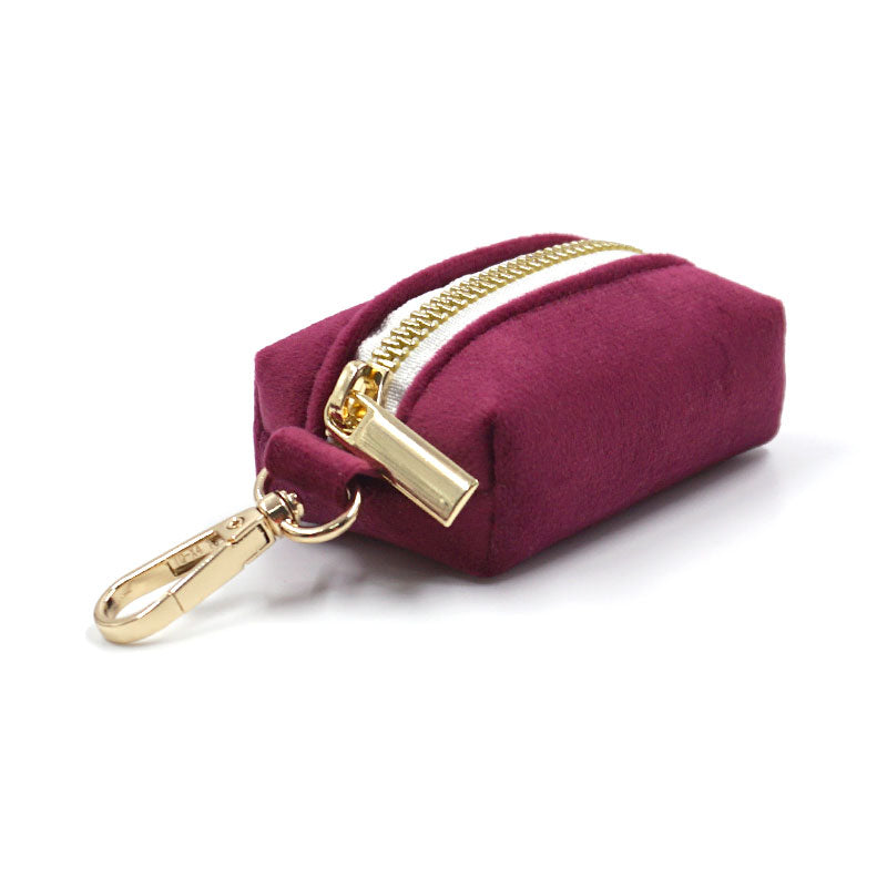 Burgundy velvet poop bag dispenser with gold zipper and clip on a white background