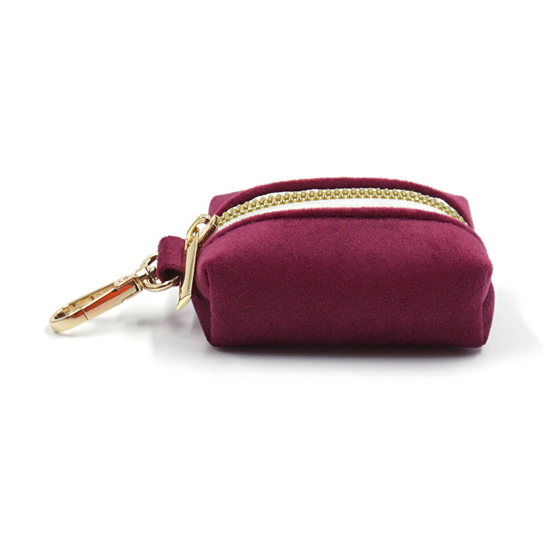 Burgundy velvet poop bag dispenser with gold zipper and clip on a white background